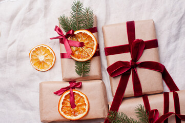 Wrapped gifts with dried orange and velvet pine branches and bows on white linen Christmas decoration diy recipe copy space flat lay top view holiday inspiration