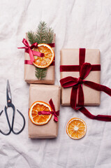 Wrapped gifts with dried orange and velvet pine branches and bows on white linen Christmas decoration diy recipe copy space flat lay top view holiday inspiration