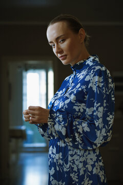Woman in blue floral dress standing by a sunlit window