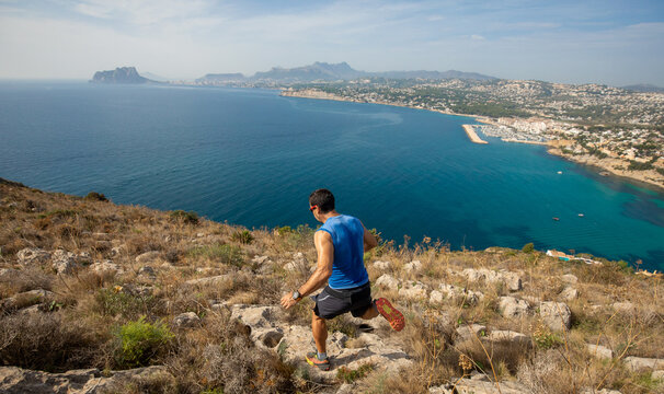 Man running down rocky hill overlooking ocean and cityscape - Powered by Adobe