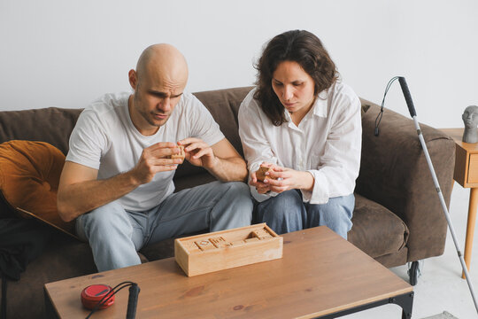 Engaged blind couple solving puzzles on a cozy living room sofa
