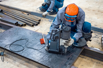 Manufacturing of metal furniture. Worker uses magnetic drilling machine. Process of creating holes...