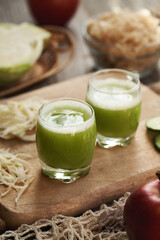 Two cups of fresh green cabbage and cucumber juice with red apples on a table