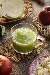 A cup of green cabbage juice with cucumber and apples on a table