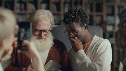 Group of young, diverse fans asking senior author to sign their copies of book, smiling and taking photos with him during launch event in library or bookstore