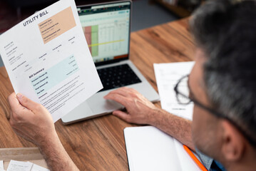 Man with glasses analyzing utility bill at a wooden desk. Financial planning and household budget...