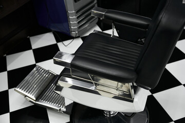 Stylish black barber chair in modern barbershop with checkered floor