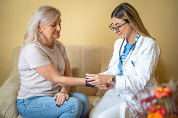 Fototapeta premium caregiver doctor examine older patient use blood pressure gauge. Young woman therapist nurse at nursing home taking care of senior elderly woman sit on sofa. Medical insurance service concept