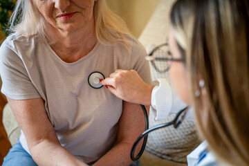 Young woman nurse doctor holding stethoscope examining old senior grandma patient check heartbeat...