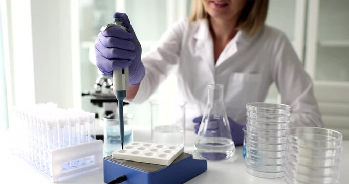 Woman doctor uses mechanical pipette dispenser in laboratory. Female physician works in clinical lab transferring solutions into microplate cells