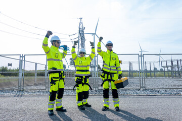 Side view three wind turbine or windmill workers or engineers stand with raise hands up to express happiness in wind turbine field near small power plant.