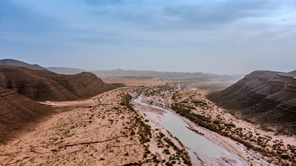 Moroccan Sahara Desert, ancient black volcanic mountains, the Sahara River Oued Ghris, stunning Acacia trees, wild camels, and desert camp,  landscape where golden sand dunes merge with green plants