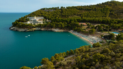 Fototapeta premium Aerial view of a bay with a small beach surrounded by hills with trees and forest.