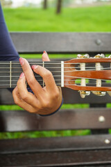 Woman Hand and Fingers on Guitar Fretboard in Green Park. Close-Up Shot.