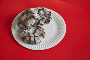 Cracked chocolate cookies on a white paper plate against a red background, close-up, homemade baking