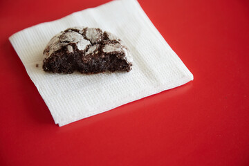 A paper napkin with one half of a chocolate cookie with cracks on a red background, close-up, half portion, strict diet, limiting sweet and pastry consumption.