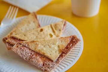 Freshly baked tortilla chips with sugar and cinnamon on a paper plate next to a glass, fork, and napkins against a yellow background, close-up.