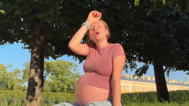 beautiful pregnant woman in 3rd trimester feels unwell outside, in the park in summer, lower back pain and hot