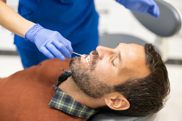 A man reclines in a dental chair during a procedure, displaying comfort and trust in the setting, as a dental professional provides attentive care.