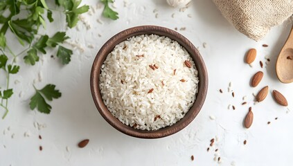 A bowl of freshly cooked rice, garnished with spices. The rice is white and fluffy, and the bowl is made of dark wood. There are fresh herbs and almonds scattered around the bowl.