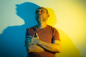 White man leaning against a wall with blue and yellow colored lights above him. Studio portrait.