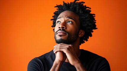 Thoughtful man with textured hair gazing at vibrant orange background