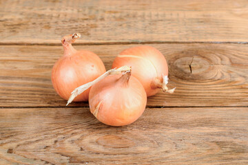 Three ripe unpeeled onions on a wooden background.