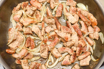 Top view of a frying pan with pieces of meat and chopped onions.