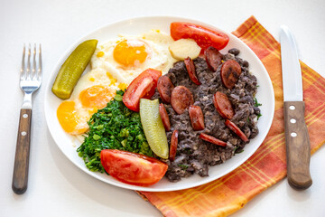Rustic, nutritious Brazilian food, black bean stew with eggs, grilled sausage, pickles and natural fermentation, kale and vegetables. Real food