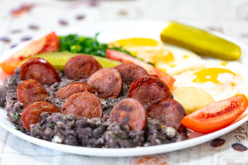 Rustic, nutritious Brazilian food, black bean stew with eggs, grilled sausage, pickles and natural fermentation, kale and vegetables. Real food