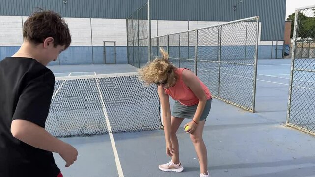 A teenager and his mother on a tennis court doing simple coordination and reflex exercises