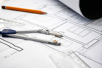 Architectural project with compass, pencil and rolled blueprints lying on construction plans of a house