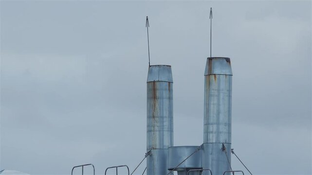 Rusty metal chimneys with lightning rods stand on a rooftop against a cloudy sky, creating an industrial landscape