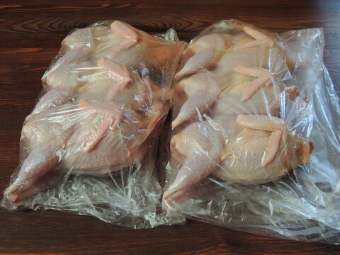 six plucked gutted quail carcasses wrapped in transparent plastic bags lie on a dark brown table, poultry farm produce, packaged poultry meat for storage and cooking