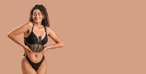 Beautiful young happy African-American woman in stylish lace lingerie on beige background