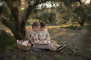 A girl and a boy in an olive grove after school, enjoying apples and reading books. A peaceful moment of relaxation and learning in nature.