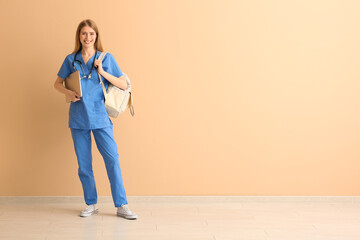Female medical intern with laptop and backpack near beige wall