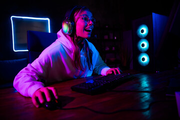 Young woman in sportswear gaming at night with neon lights and digital equipment in casual style playing video games online