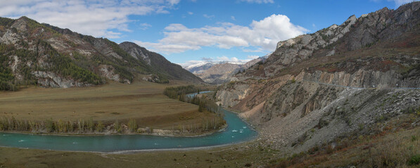 Wide panorama of mountain gorge with a stream in the middle. Golden autumn forest along the water stream. Mountain slopes are sleep with a red tint like on another planet like a Martian landscape.