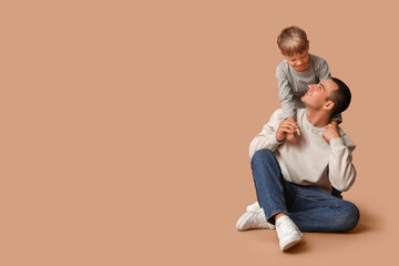 Happy father and his little son sitting on beige background
