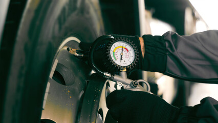 Checking Tire Pressure with a Manual Gauge. A close-up of a gloved hand using a manual tire...