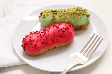 Plate with tasty glazed eclairs and fork on light background