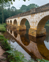 Fototapeta premium Stone bridge reflecting in calm river water.