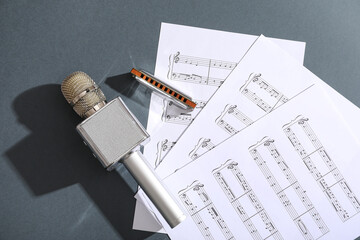 Harmonica, microphone and music sheets on dark background