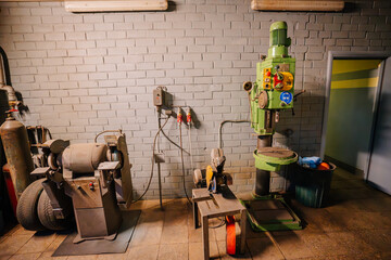 Industrial workshop with grinding machine, drill press, and other equipment against a brick wall,...