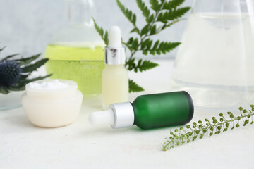 Bottles of products, Laboratory glassware with samples and ingredients for preparing natural cosmetics on white table near grunge wall
