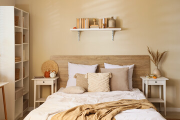 Interior of modern bedroom with comfortable bed, bedside table and pumpkins