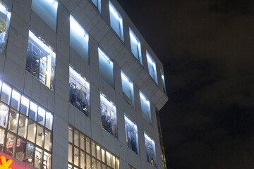 Fototapeta premium The urban buildings exterior features numerous lit windows at night, showcasing striking modern architecture that reflects vibrant city life, bustling with activity and energy