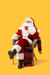 Santa Claus with letters and cocoa sitting in armchair on yellow background