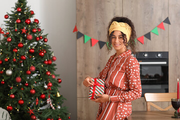 Fototapeta premium Young African-American woman with gift box celebrating Kwanzaa in kitchen